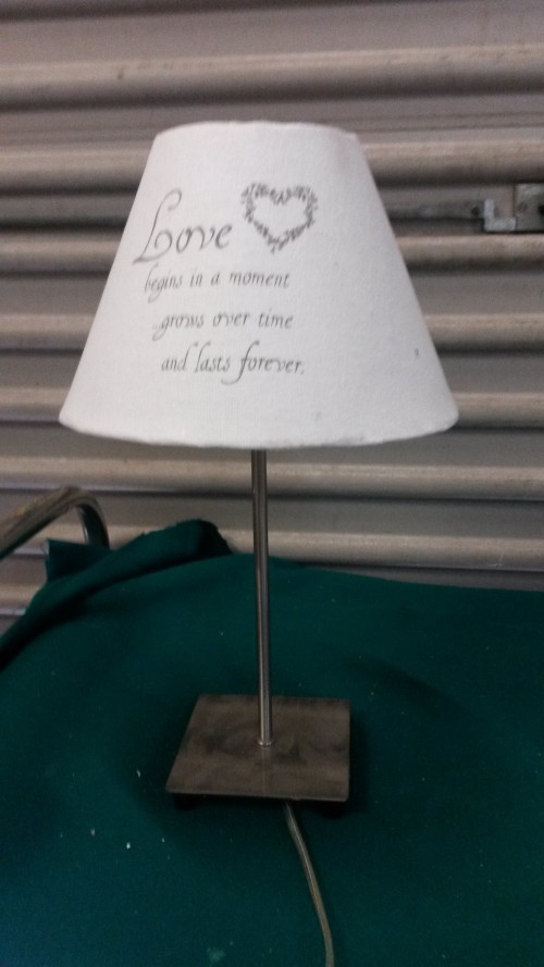 Tafellamp, metalen voet en witte kap met tekst: Love begins