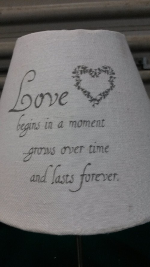Tafellamp, metalen voet en witte kap met tekst: Love begins